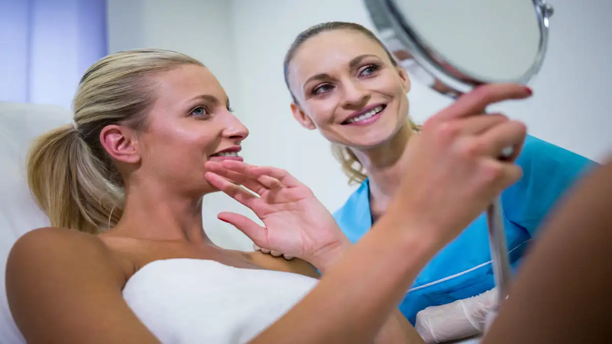 a imagem mostra uma paciente se olhando no espelho após o procedimento de harmonização facial
